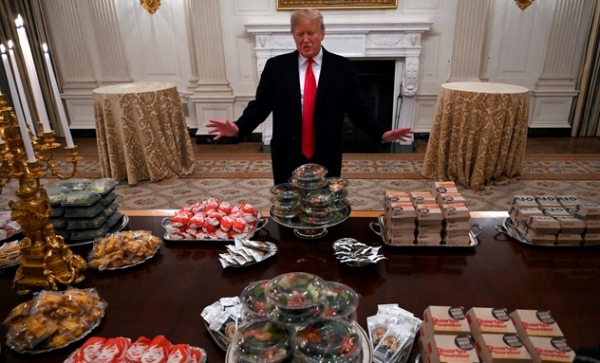트럼프 대통령이 백악관에서  미국 대학 풋볼 챔피언에 오른 클렘슨 대학 선수단을 맞기 전 햄버거 상자들이 쌓여있는 테이블 앞에 서있다.