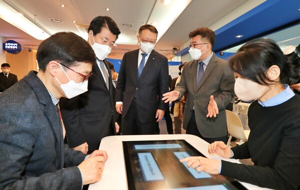 우리은행 정진완 은행장(가운데), 서강석 송파구청장(가운데 왼쪽)이 Woori 어르신 IT 행복배움터 송파점 개소식에 참여해 해피테이블(인지능력개선 디지털기기)에 대한 설명을 듣는 모습. 우리은행 제공.