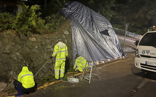 남구청이 집중호우로 붕괴 위험이 있는 도로변 경사면에 방수포를 덮고 있다./남구
